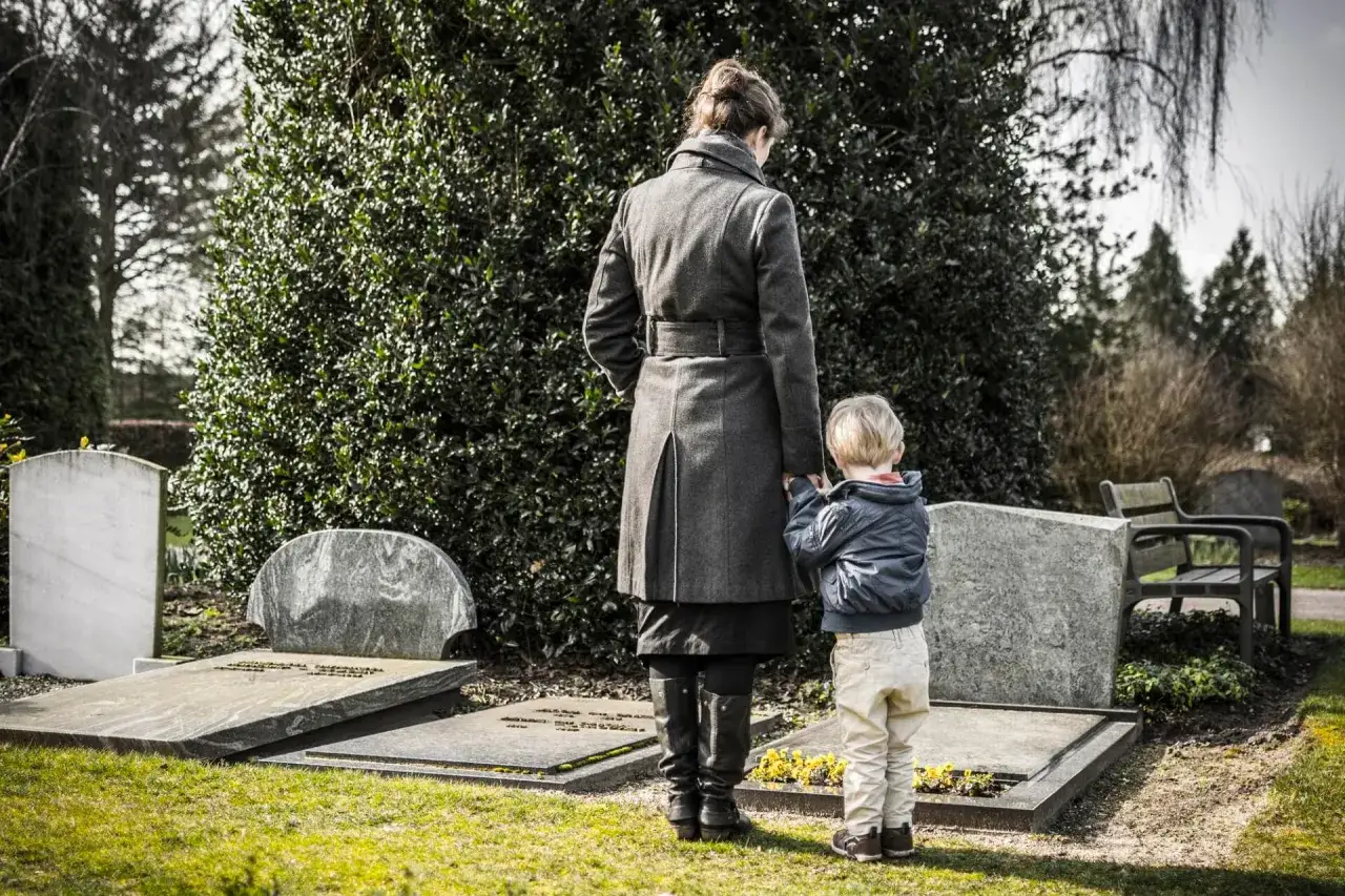 Kobieta i dziecko stoją przy grobie, symbolizując etapy żałoby.