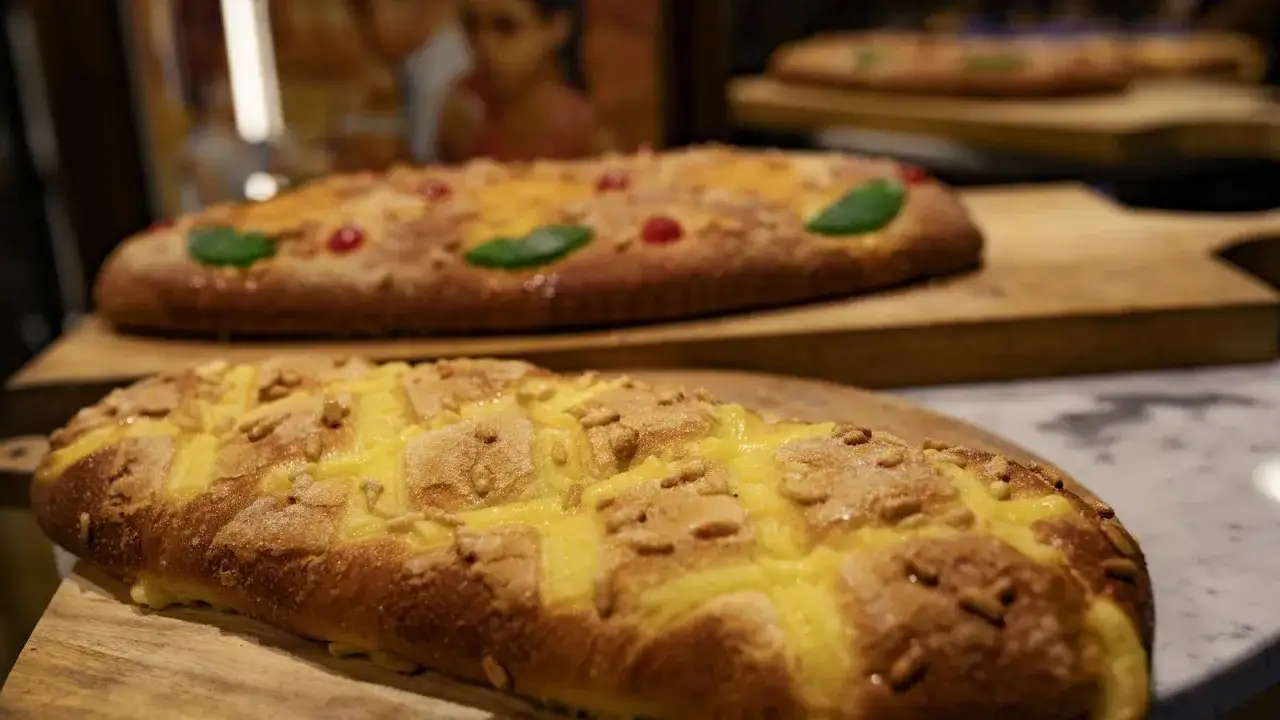 Dos cocas de San Juan decoradas con piñones y crema, una con cerezas y frutas escarchadas.