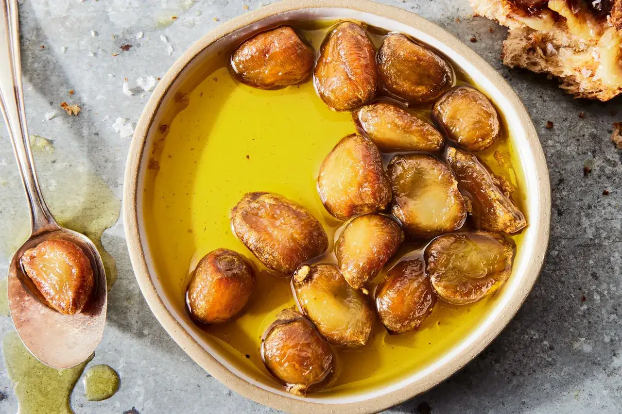 Golden, tender garlic cloves swimming in olive oil, a delicious result of how to make garlic confit. A spoon holds one perfect clove.