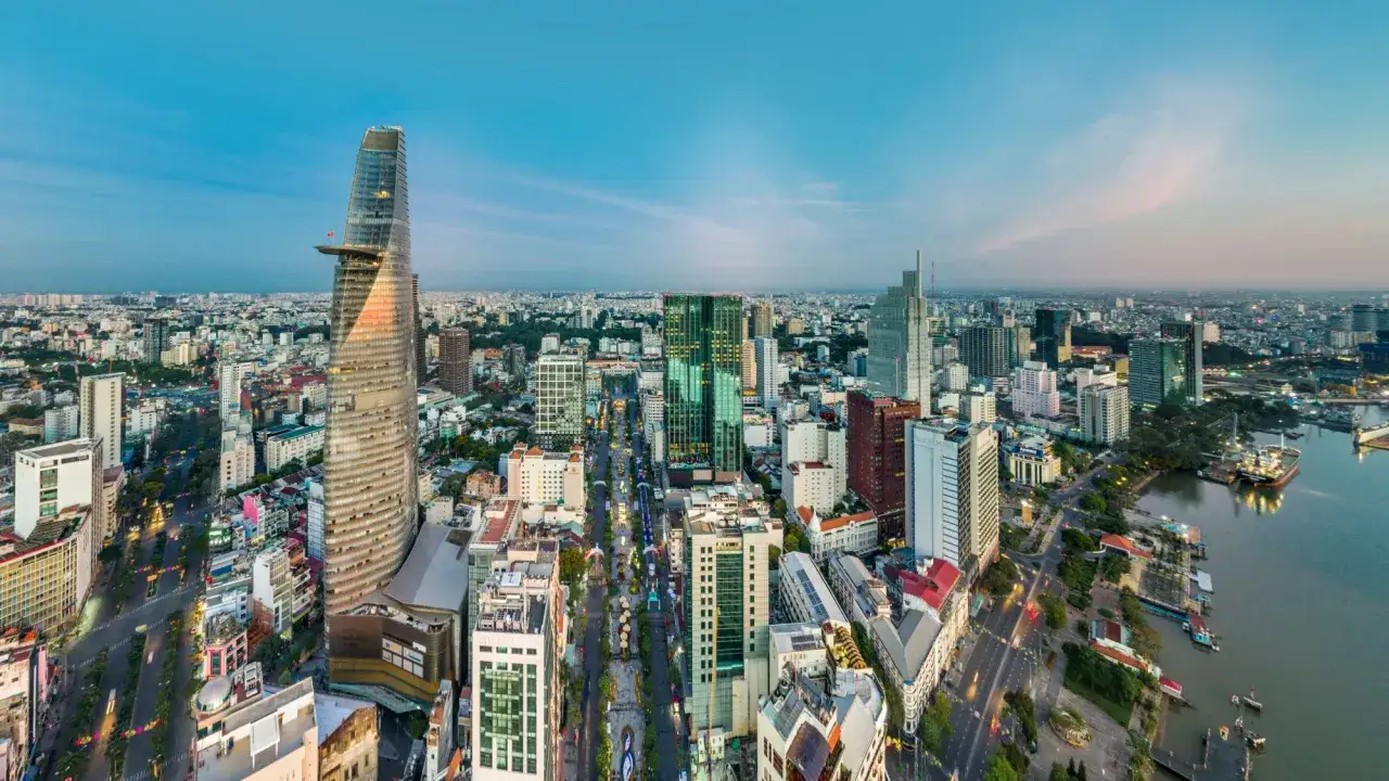 Panorama miasta Ho Chi Minh o zachodzie słońca. Widać drapacze chmur, ruchliwe ulice i rzekę z statkami.
