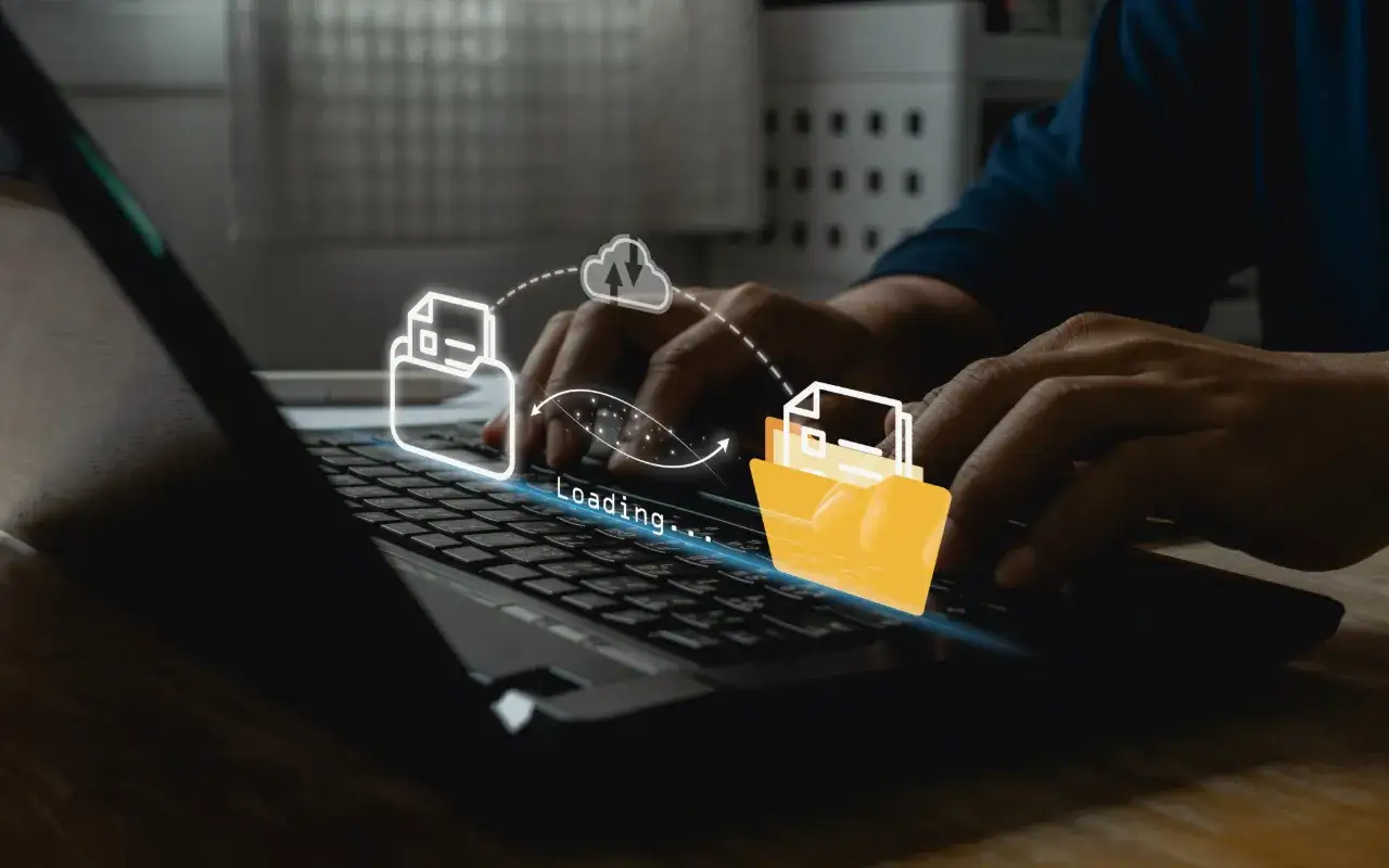 Hands typing on a laptop, illustrating the process to transfer OneDrive to Google Drive with animated icons showing data moving between cloud storage.