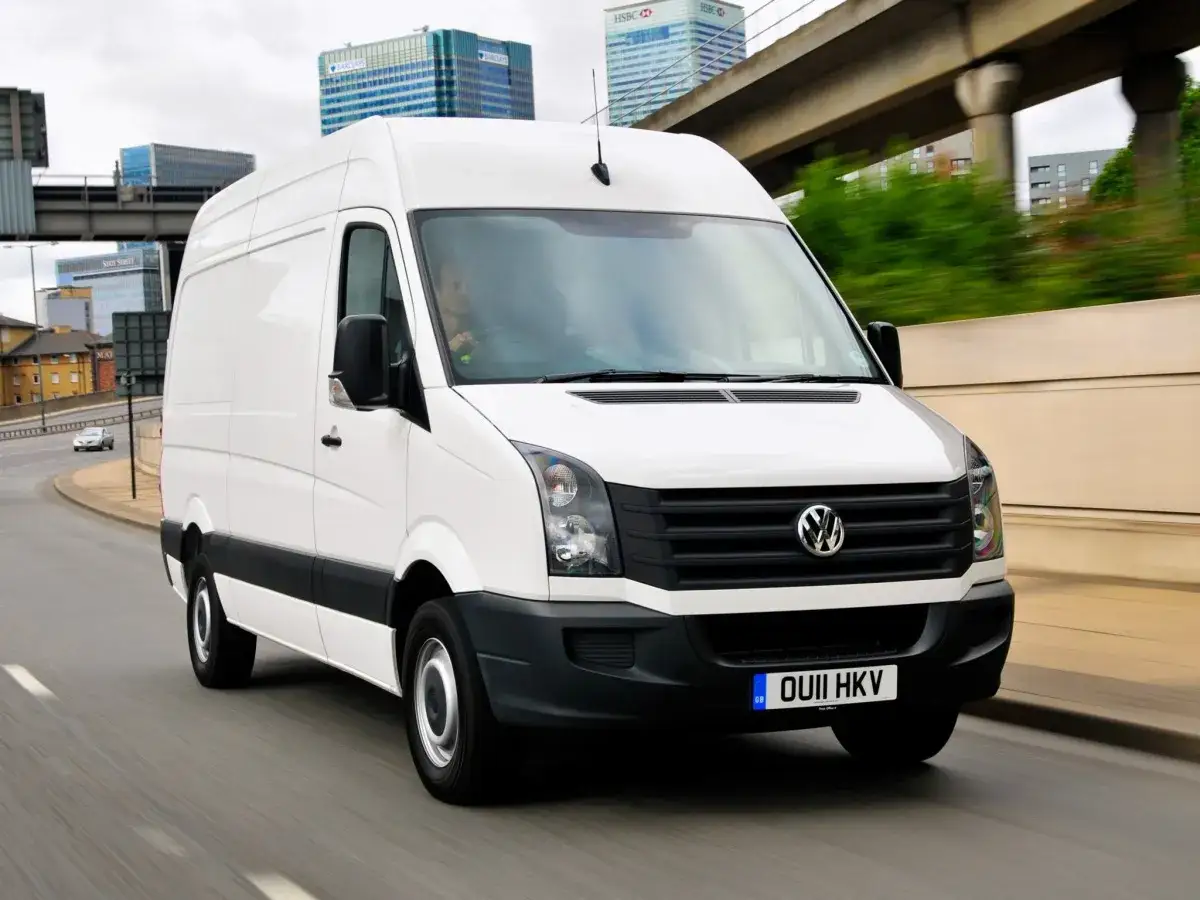 Biały Volkswagen Crafter 2.5 TDI w ruchu miejskim, z widocznym kierowcą za kierownicą.