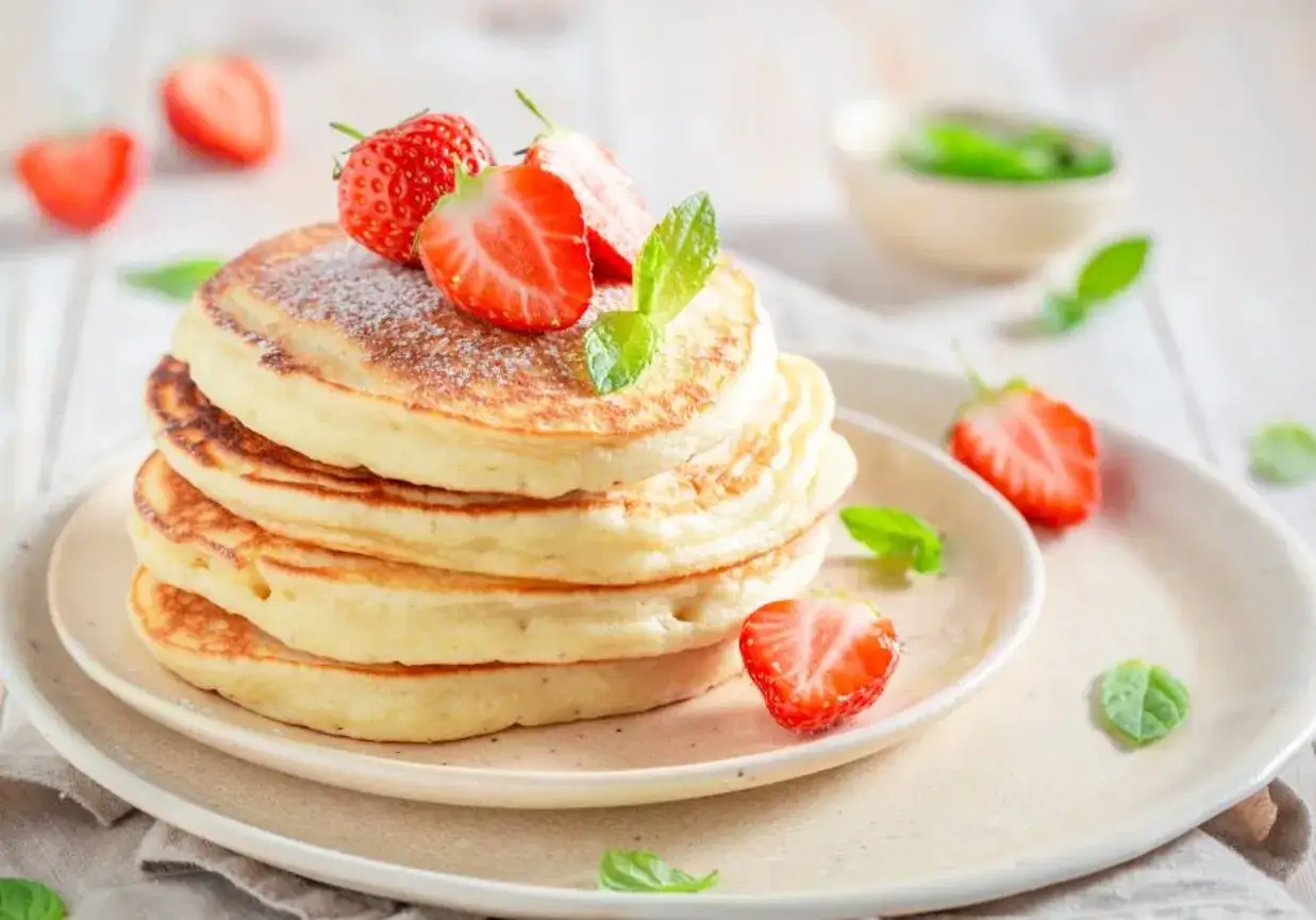 Puszyste pancakes na mleku, udekorowane świeżymi truskawkami i listkami mięty, kuszą swoim wyglądem.