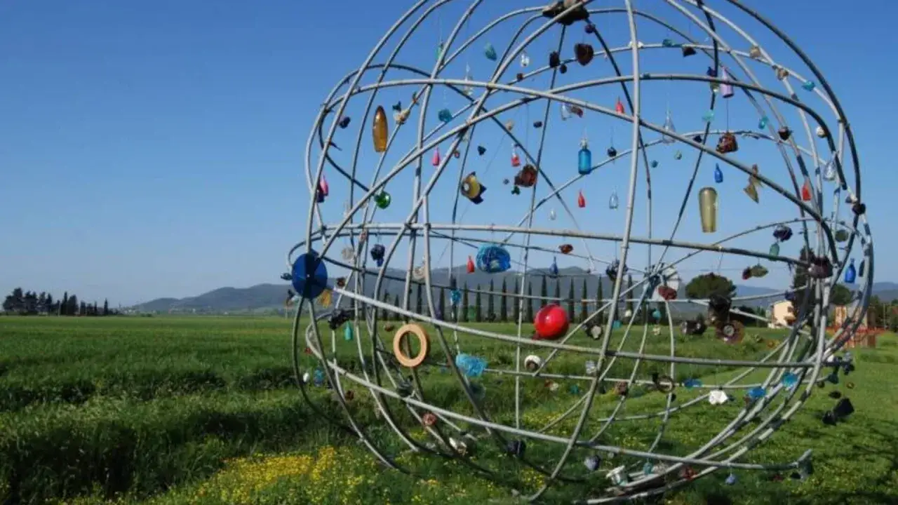 Scultura sferica con oggetti colorati appesi, in un prato verde. Un ricordo del **giardino viaggio di ritorno**.