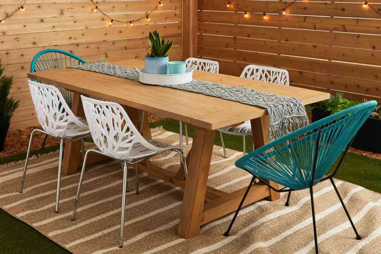 Ein rustikaler Holztisch, perfekt zum **gartentisch selber bauen**, umgeben von modernen St&uuml;hlen auf einer gestreiften Matte.