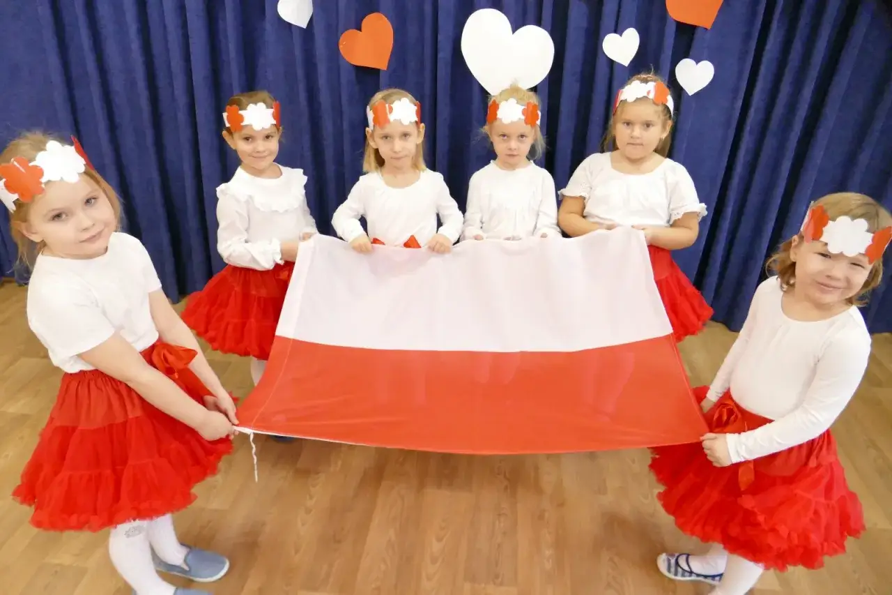 Dzieci w strojach biało-czerwonych trzymają polską flagę, celebrując Dzień Niepodległości.