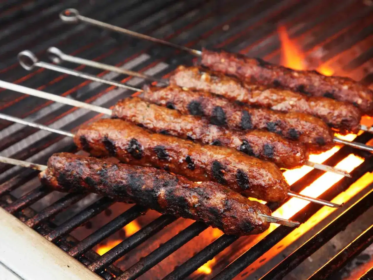 Saftige Seekh Kebabs brutzeln auf dem Grill. Die Flammen lecken an den Fleischspießen und verströmen einen unwiderstehlichen Duft.