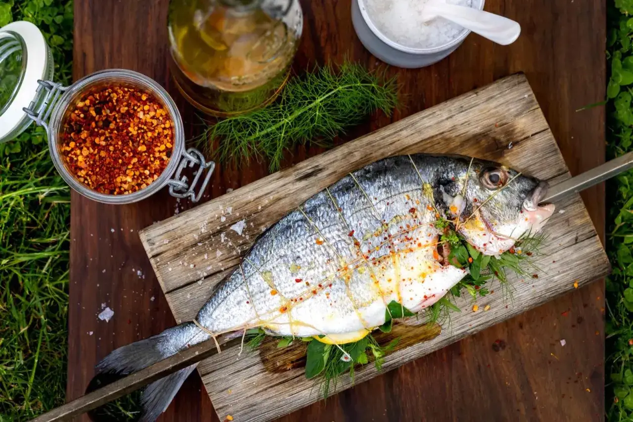En hel, silverf&auml;rgad fisk, redo f&ouml;r grillen. Kryddad med chili, &ouml;rter och citron, p&aring; en tr&auml;planka.