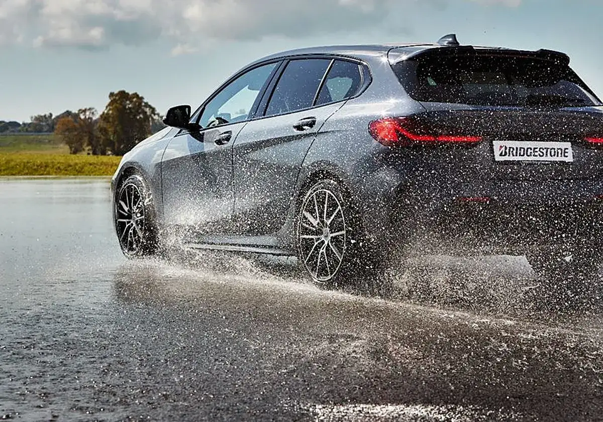 Un coche gris salpica agua al circular a velocidad excesiva sobre un asfalto mojado.