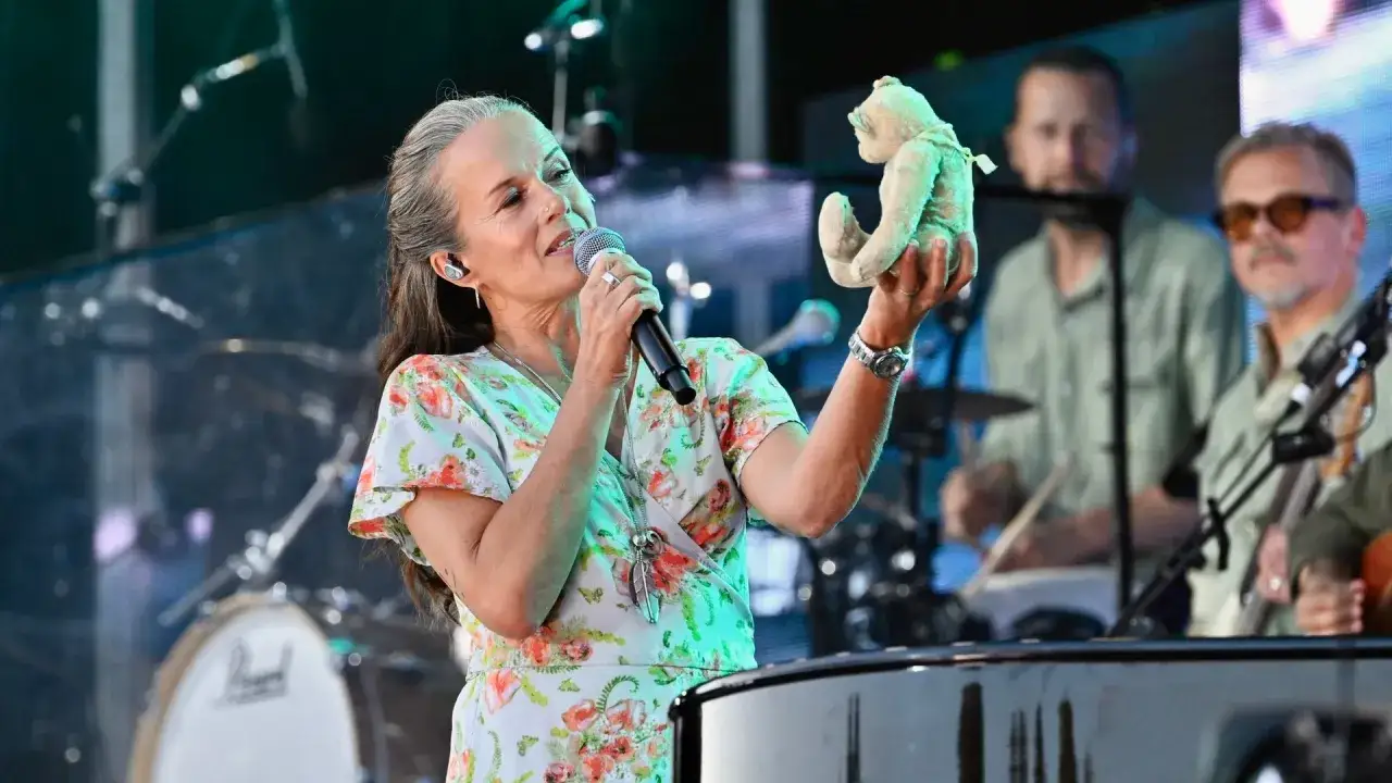 Malin Berghagen sjunger med en nallebjörn i handen på scenen, ackompanjerad av musiker.
