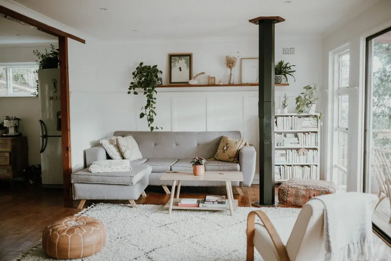 Ett vardagsrum med gr&aring; soffa, tr&auml;bord och bokhylla. V&auml;xter och konst ger liv &aring;t rummet, allt i en stil av skandinavisk minimalism.