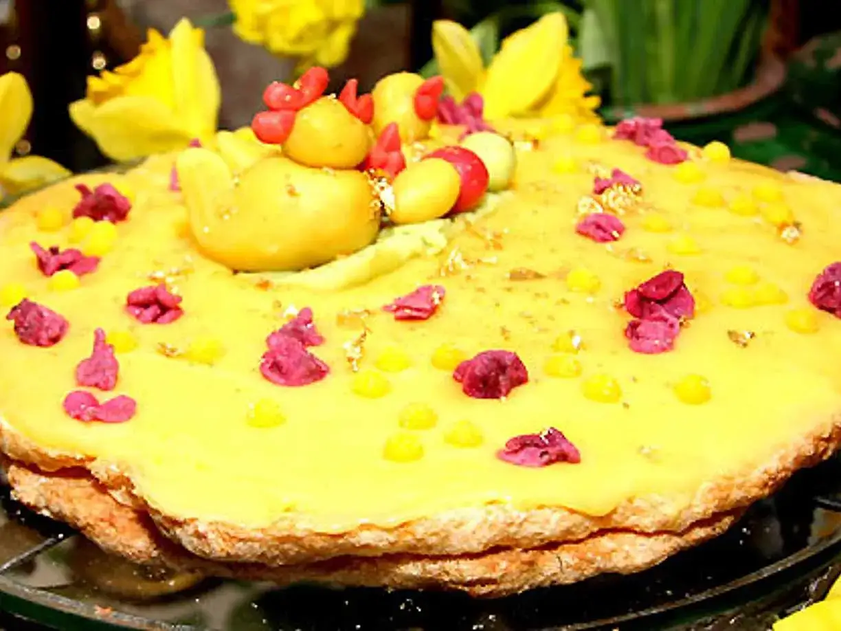 En gul tårta med en kycklingfigur på toppen, dekorerad med rosa blommor och gula prickar. En perfekt