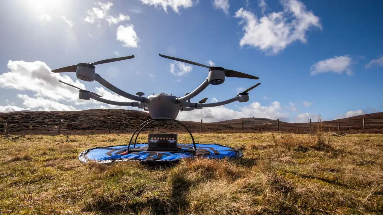 A grey drone sits on a landing pad in a grassy field, ready for search and rescue missions.