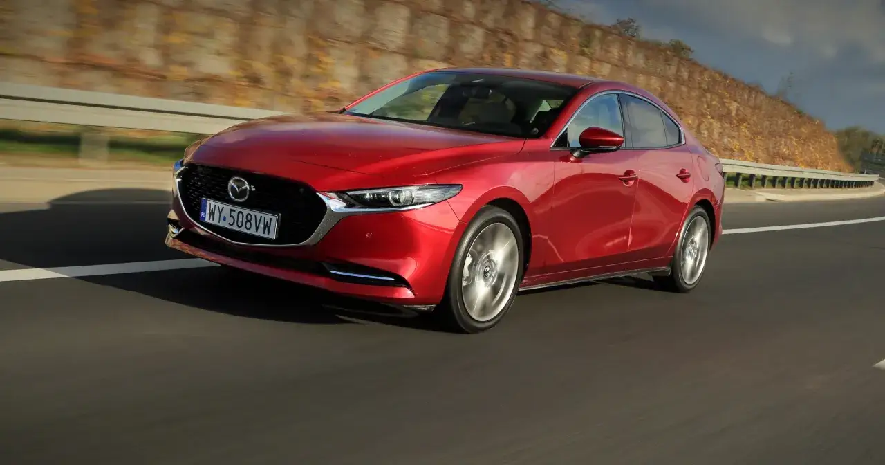 Czerwona Mazda 3 sedan w ruchu na drodze.