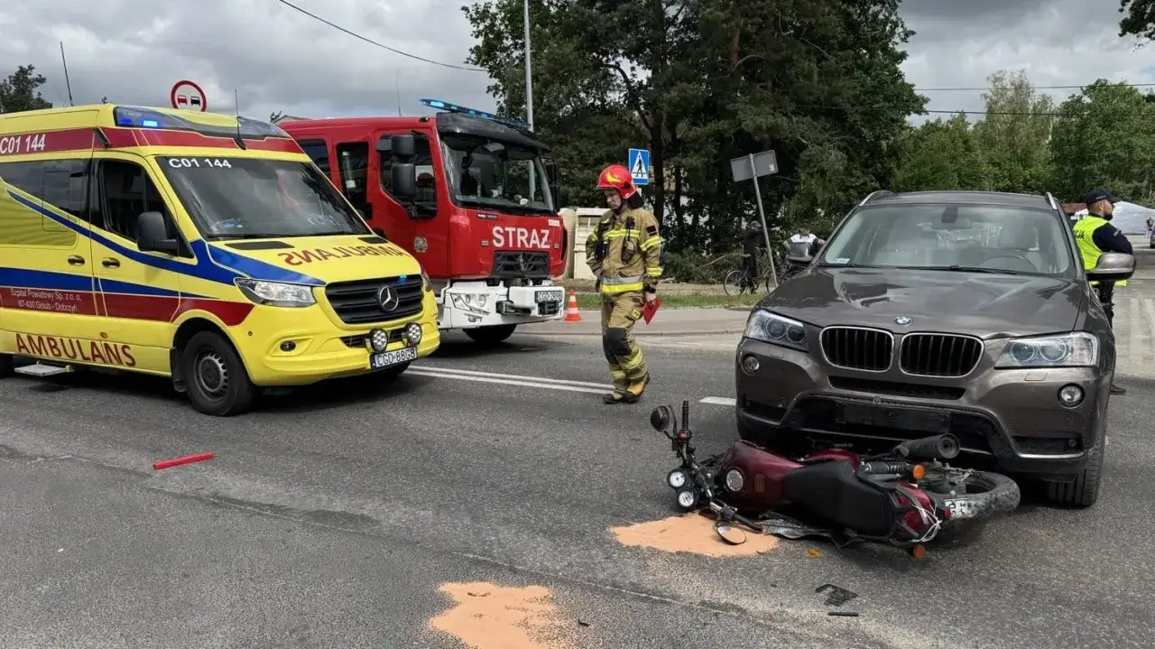 Wypadek drogowy z udziałem motocykla, samochodu i pojazdów uprzywilejowanych: straży pożarnej i ambulansem. Na miejscu pracują służby.
