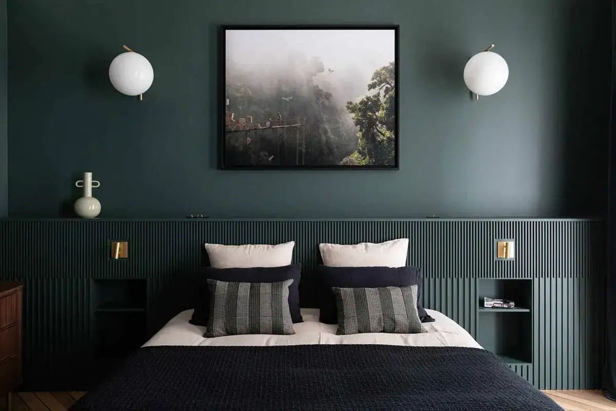 Une chambre moderne avec une tête de lit lambrissée vert forêt. Le tableau abstrait au-dessus du lit et les appliques murales sphériques complètent la deco peinture chambre.