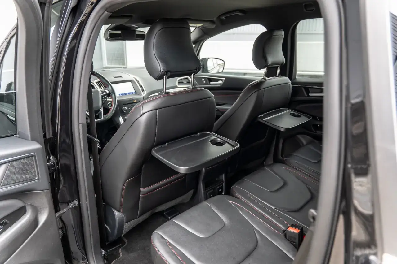 Wnętrze Ford S-Max: czarne skórzane fotele z czerwonymi przeszyciami, rozkładane stoliki dla pasażerów z tyłu.