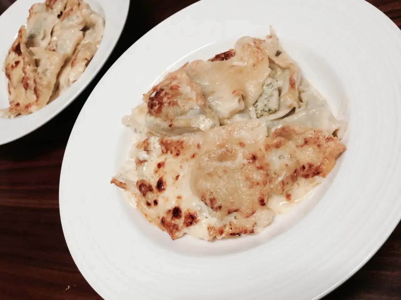 Ricos ravioles de Royan gratinados, con queso derretido y bordes dorados, servidos en un plato blanco.