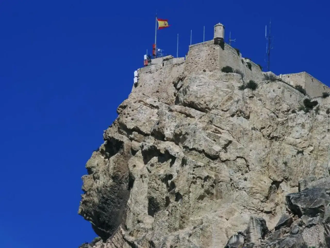 La cara del moro alicante, una roca con forma de perfil humano, corona el castillo. Bandera española ondea.