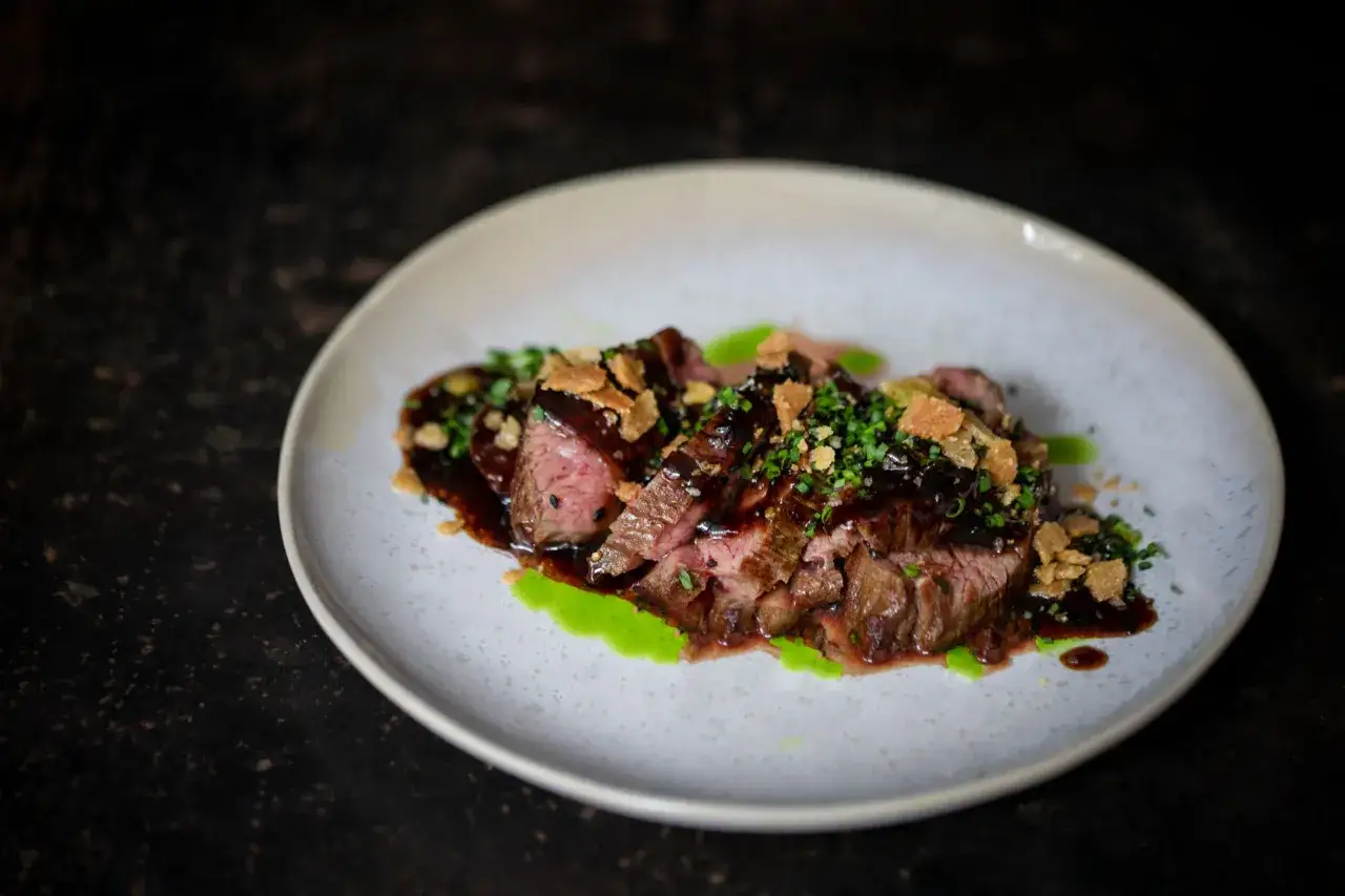 Saftiges Rindersteak, &uuml;bergossen mit dunkler Sauce und garniert mit knusprigen Kr&uuml;meln und Kr&auml;utern. Ein Hauch von schwarzem Knoblauch verleiht dem Gericht eine besondere Note.