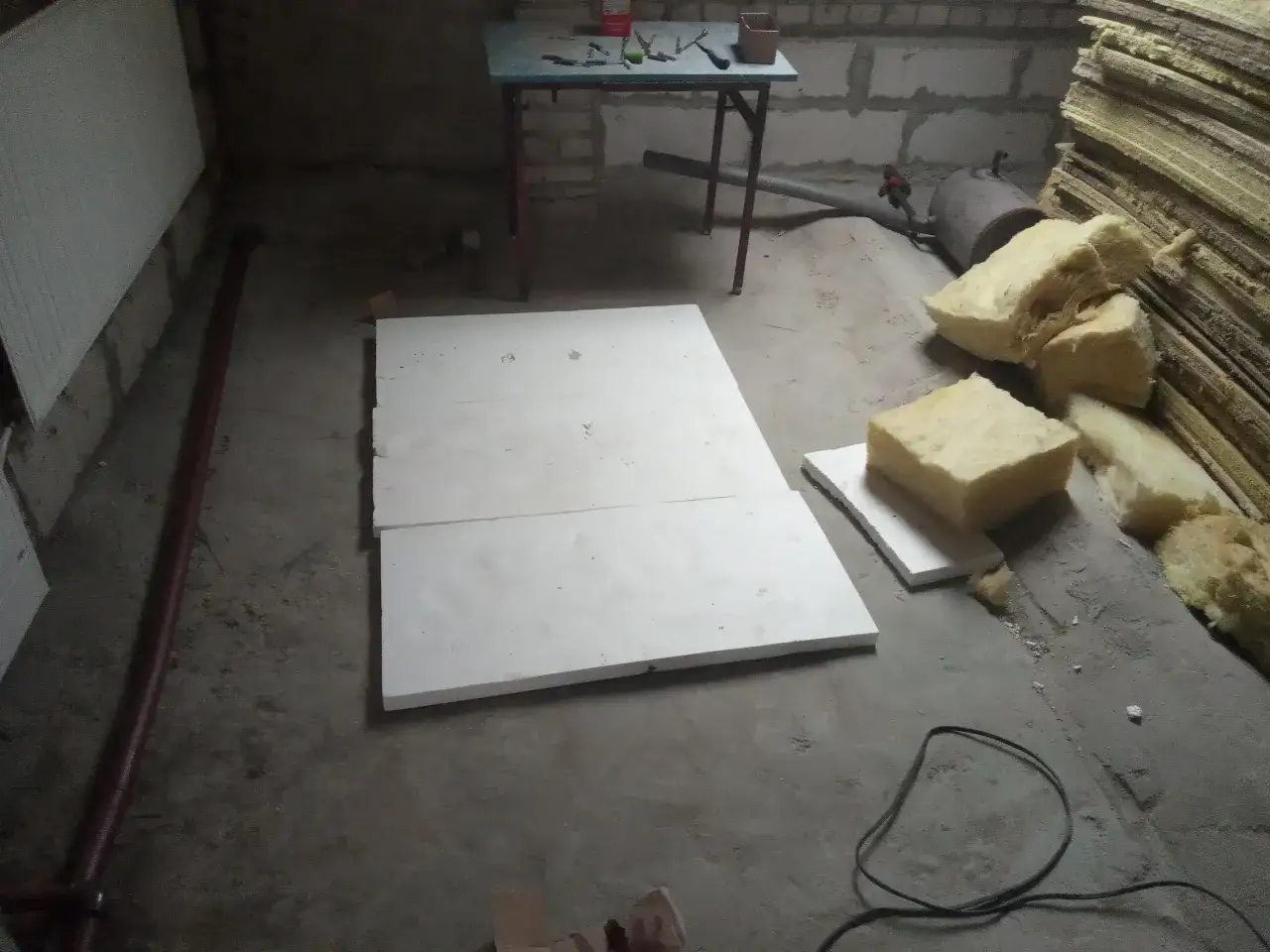 Płyty styropianu czekają na ułożenie na strychu. Obok leżą materiały izolacyjne i narzędzia.