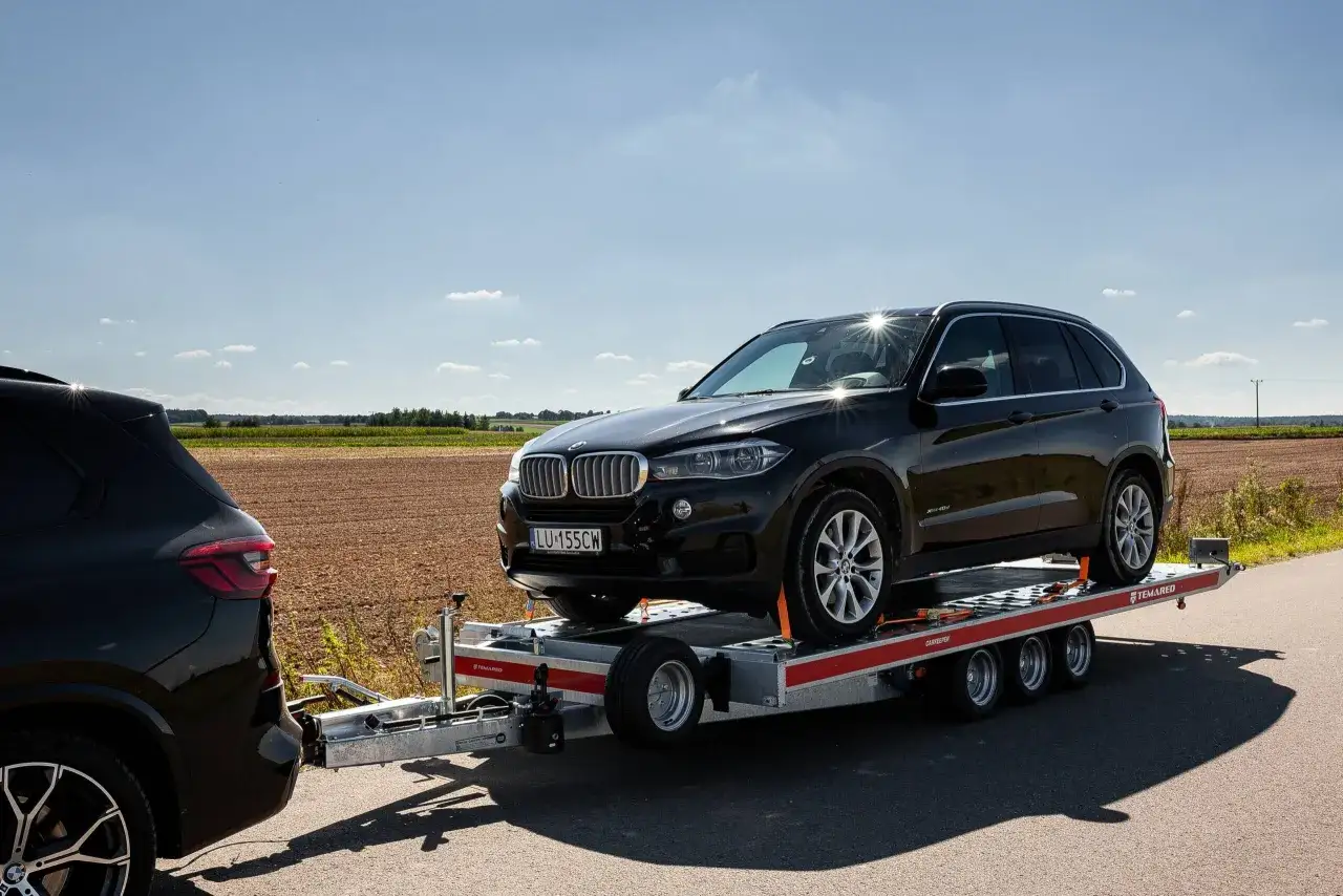 Czarny SUV na lawecie, gotowy do podróży. Zastanawiasz się, ile można jechać z przyczepą na autostradzie? Sprawdź przepisy!