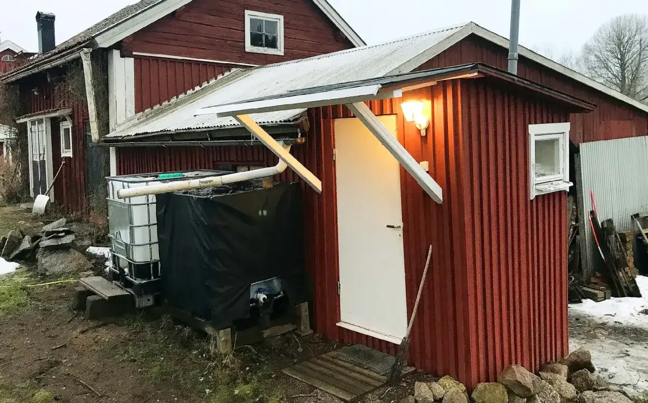 En röd bod med vit dörr, en del av ett projekt för att bygga utedass. Vattentankar syns bredvid.