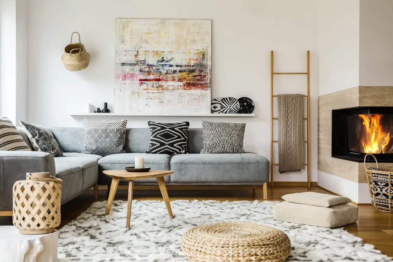 Salon cosy avec canapé gris, tapis blanc, cheminée et tableau abstrait. Pour un style doux, pensez à comment faire du blanc cassé avec des touches naturelles.