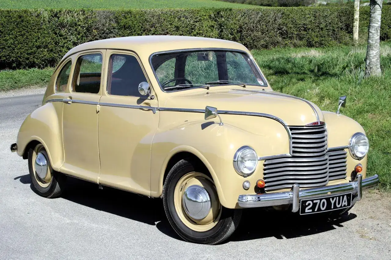 En ljusgul Jowett Javelin från 1950-talet står parkerad vid en grönskande häck.