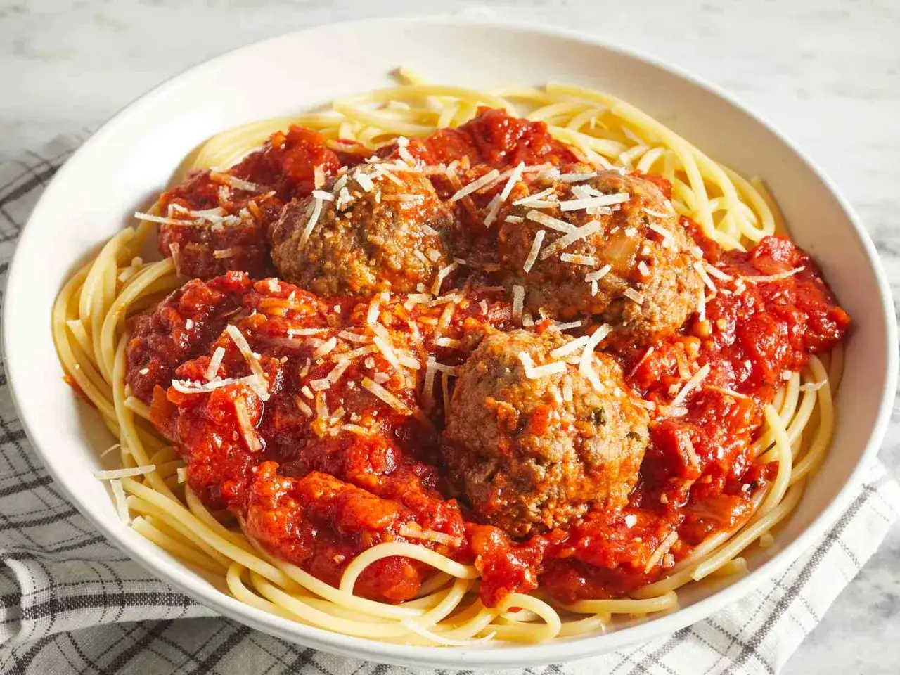 En sk&aring;l med spaghetti och k&ouml;ttbullar i tomats&aring;s, toppad med riven ost. Enkel guide f&ouml;r como hacer albondigas.