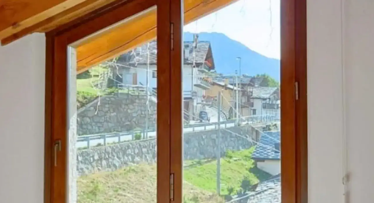 Finestra in legno con vista su un villaggio alpino. Ideale per capire come scegliere infissi che si integrino con il paesaggio.