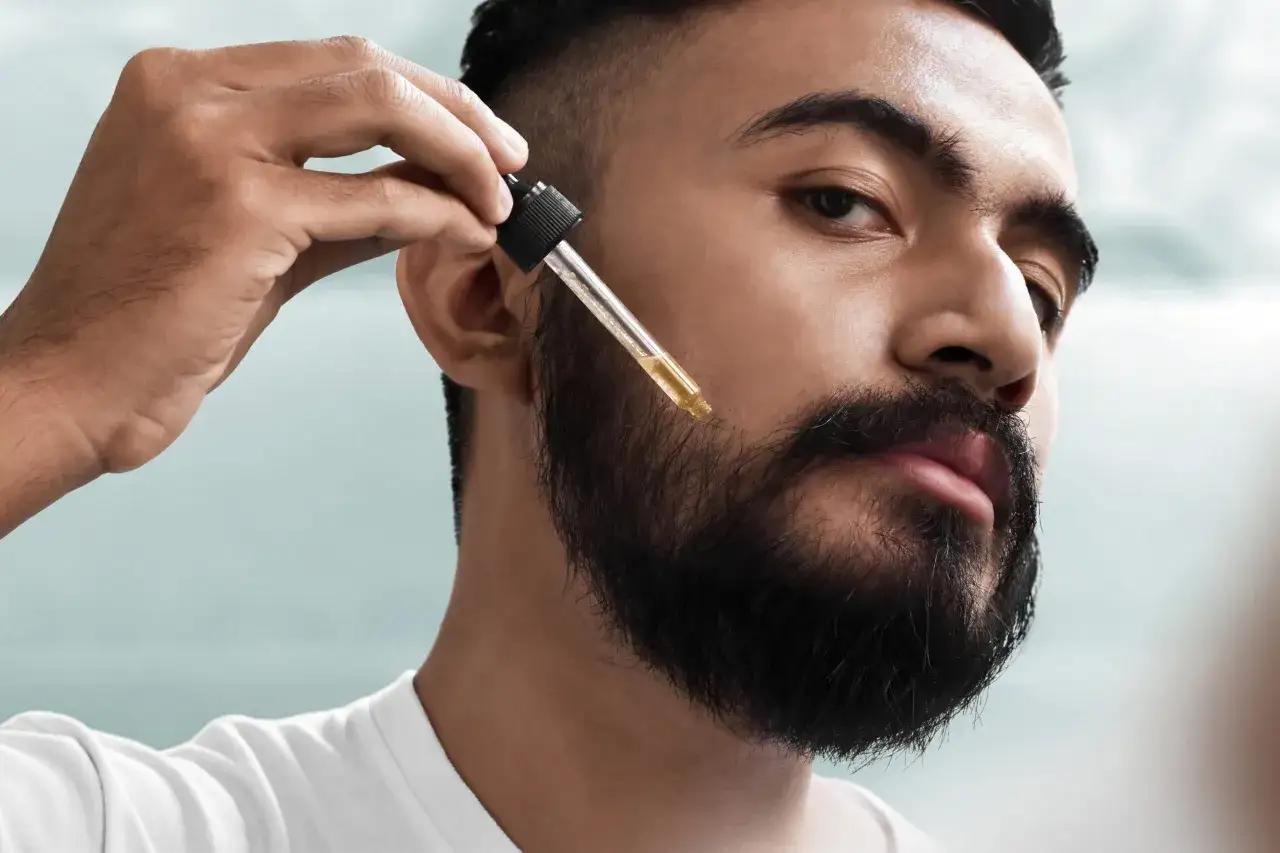 Hombre aplicando aceite con gotero en su barba. Un paso esencial para el cuidado y crecimiento de la barba con minoxidil.