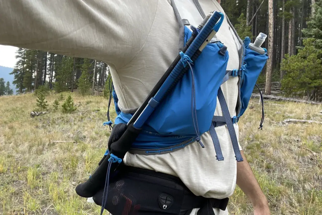 Jak przypiąć kijki do plecaka: niebieskie uchwyty i sznurki stabilizują kijki trekkingowe na plecaku biegowym.