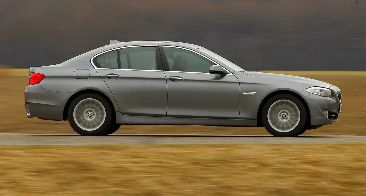 Szare BMW F10 z 2010 roku w ruchu, z widocznym kierowcą za przyciemnianą szybą.