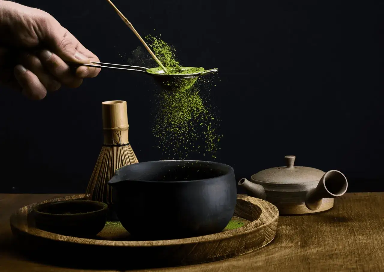 Feines Matcha-Pulver rieselt durch ein Sieb in eine Schale. Die Zubereitung für die positive matcha wirkung darm.