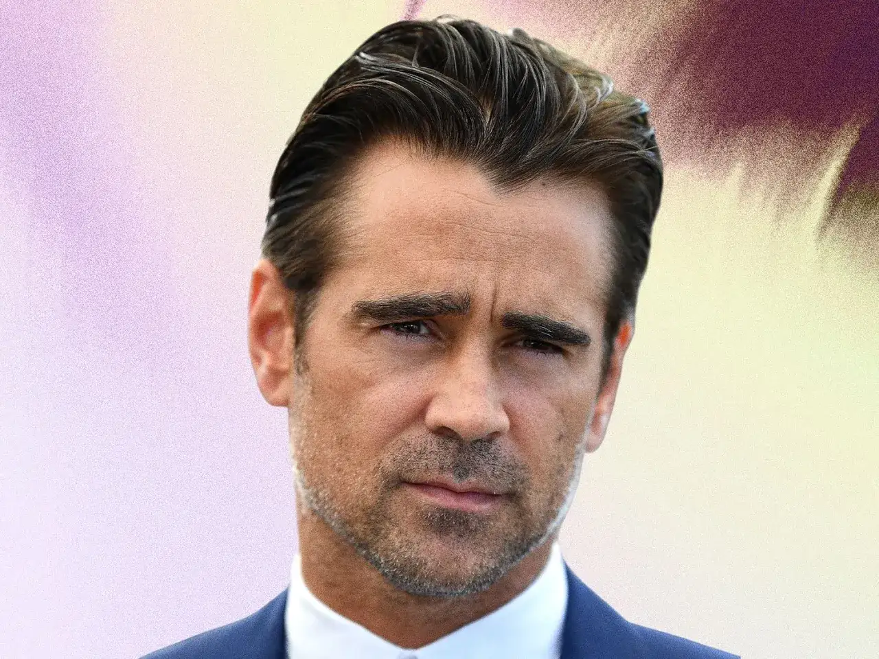 Colin Farrell z idealnie ułożonymi włosami w stylu slickback, w granatowym garniturze, patrzy prosto w obiektyw.