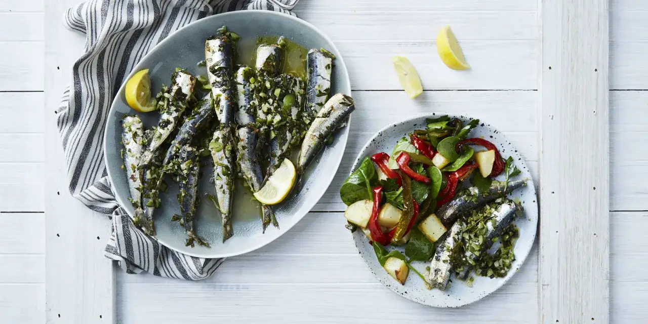 Deux assiettes de sardines grillées, l'une avec une salade de poivrons et pommes de terre, l'autre nature, garnies de citron et d'herbes. Un accompagnement sardines grillées parfait.