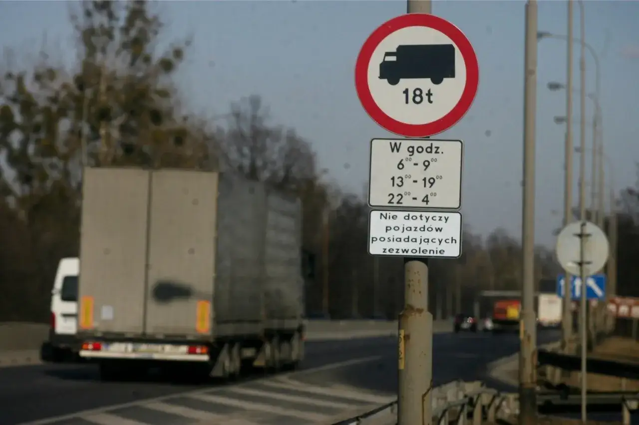 Znak zakazu wjazdu dla tirów powyżej 18 ton, z wyłączeniem godzin 6-9, 13-19 i 22-4, chyba że pojazd posiada zezwolenie.