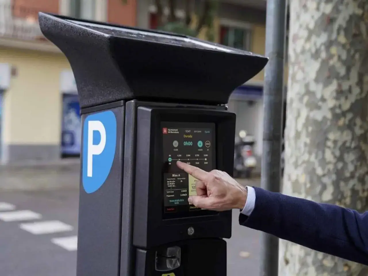 Un hombre usa un parqu&iacute;metro para el pago de la zona azul en Barcelona. La pantalla muestra opciones de duraci&oacute;n y tarifas.