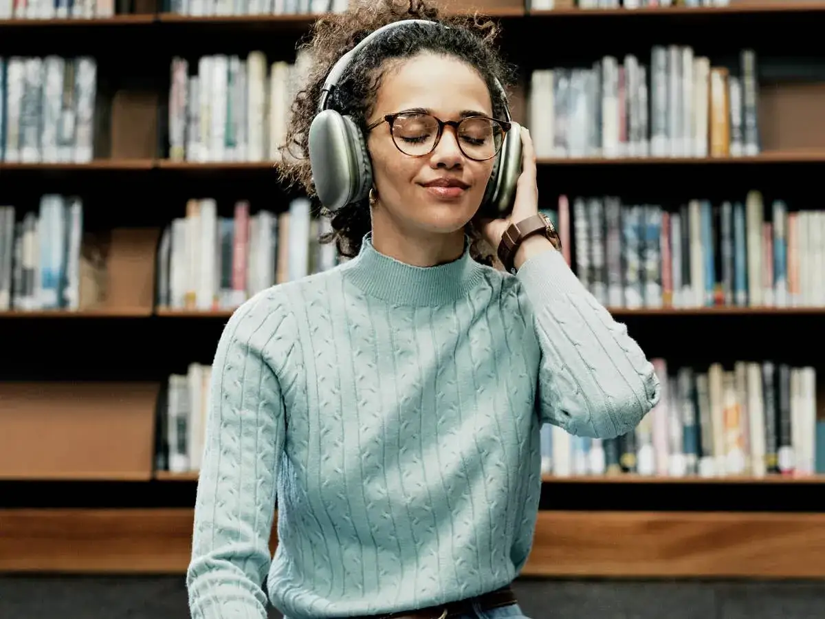 Kobieta w okularach i słuchawkach cieszy się najlepszymi audiobookami w bibliotece.