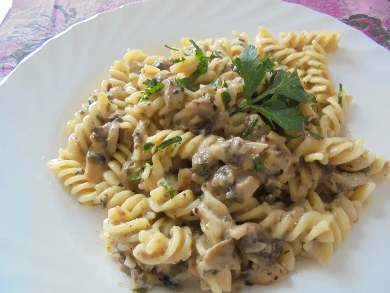 Fusilli w kremowym sosie pieczarkowym, udekorowane świeżą natką pietruszki. Pyszne danie gotowe do podania.