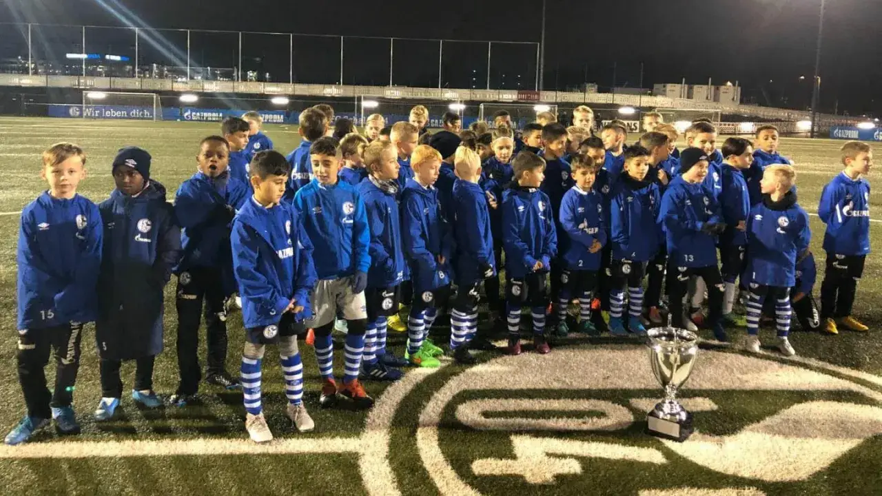 Die **Schalke U10** feiert einen Sieg mit ihrem Pokal. Die jungen Fußballer tragen stolz ihre blauen Trikots.