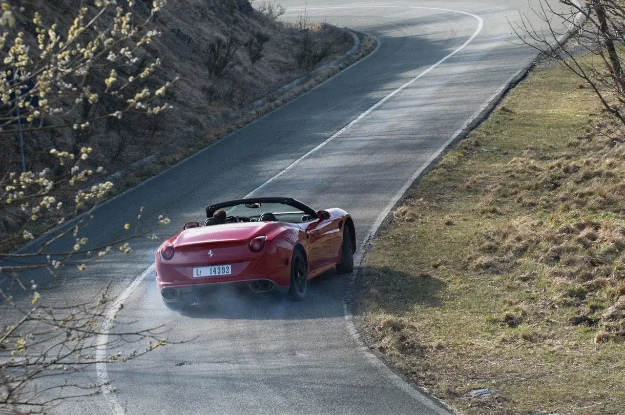 Czerwone Ferrari California z dymiącymi oponami na zakręcie górskiej drogi.