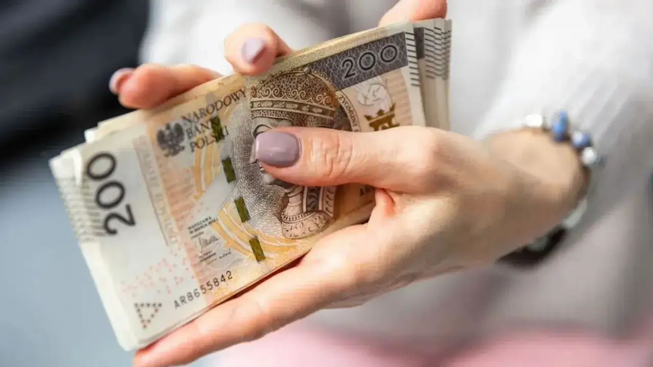 Dłonie trzymają plik banknotów 200 zł. Zastanawiasz się, co oznacza zawieszenie renty? To może być trudne, gdy pieniądze są tak ważne.