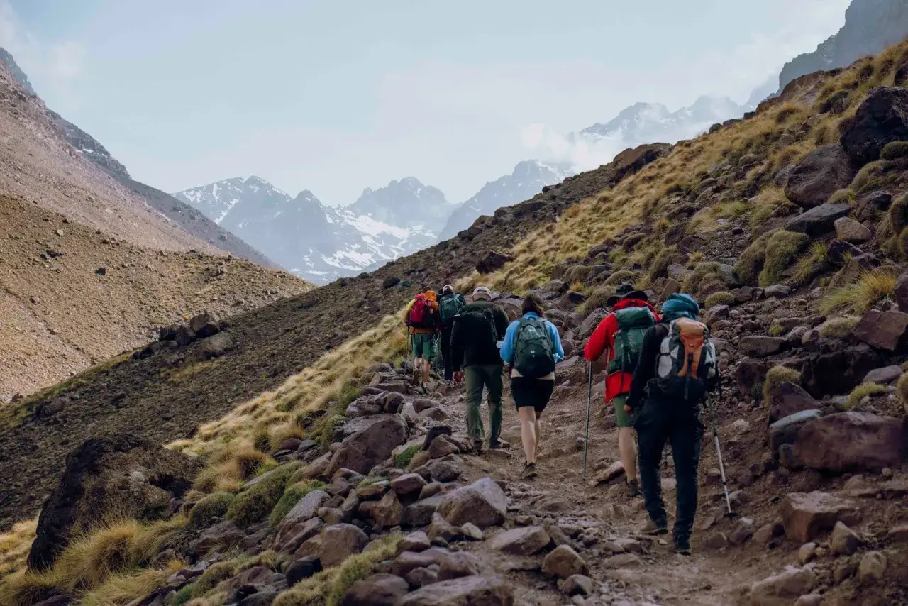 Grupa turystów wędruje kamienistym szlakiem w górach Maroka, zbliżając się do Jebel Toubkal.