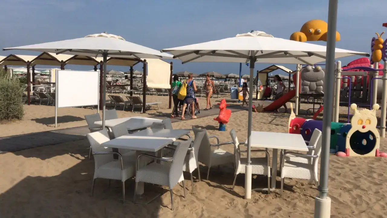 Ombrelloni, tavoli e sedie sulla sabbia dorata della regina beach Cattolica, con un'area giochi colorata sullo sfondo.