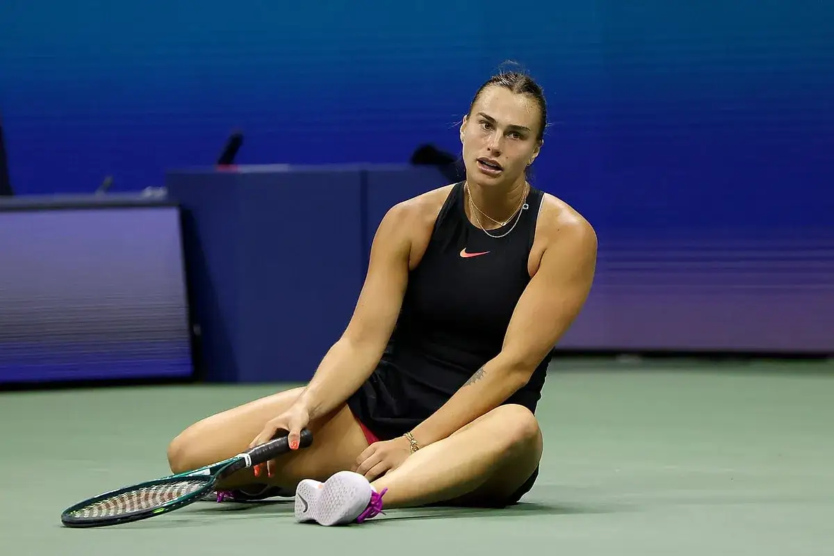 Tenisistka siedzi na korcie, trzymając rakietę. Zmęczona, ale zdeterminowana, walczy o każdy punkt w turnieju WTA 1000.