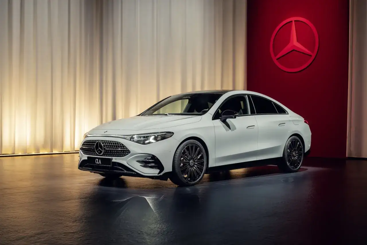 Biały Mercedes CLA 180 z czarnymi felgami prezentuje się elegancko na tle czerwonej ściany z logo marki.