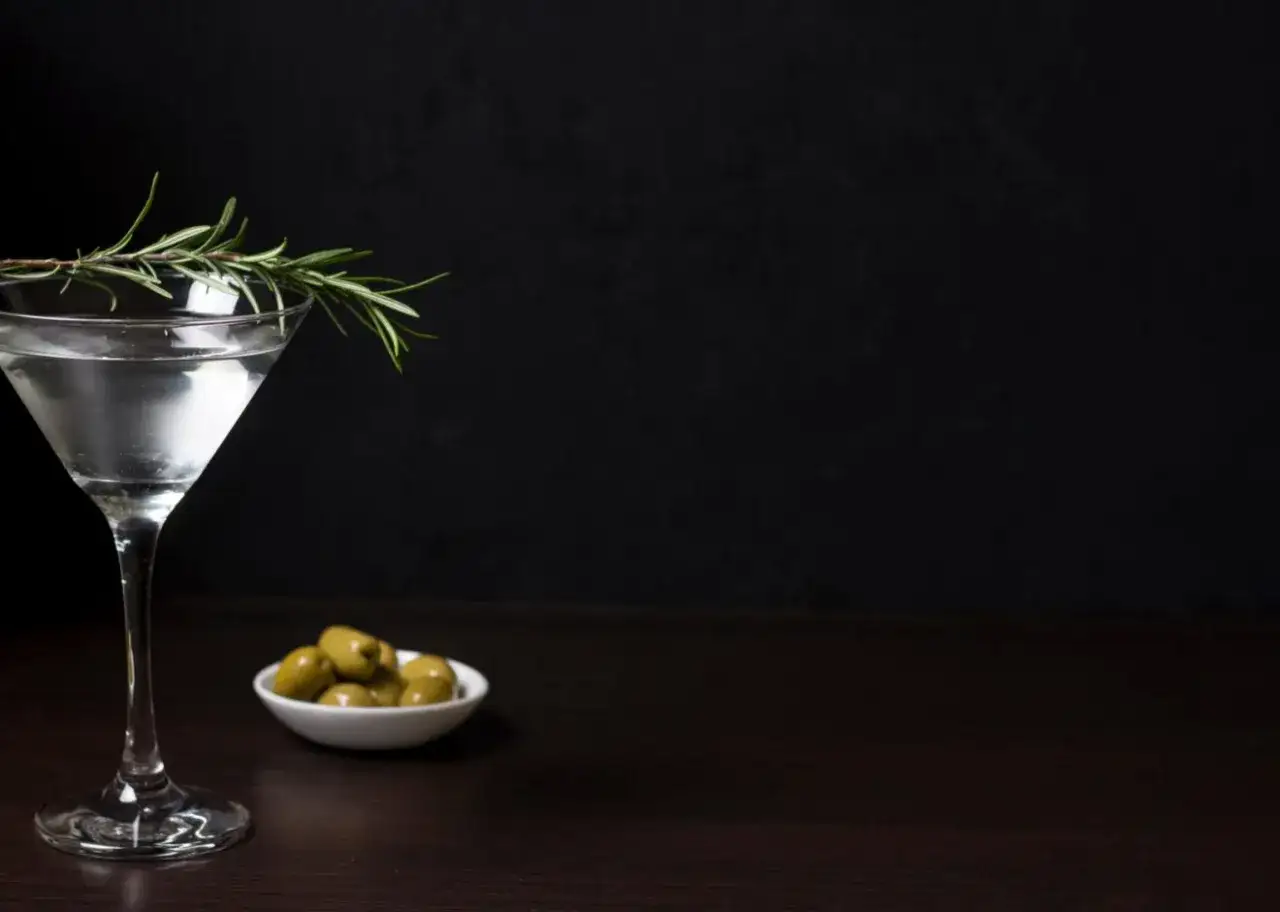 Elegancki dirty martini z gałązką rozmarynu i oliwkami na ciemnym tle.