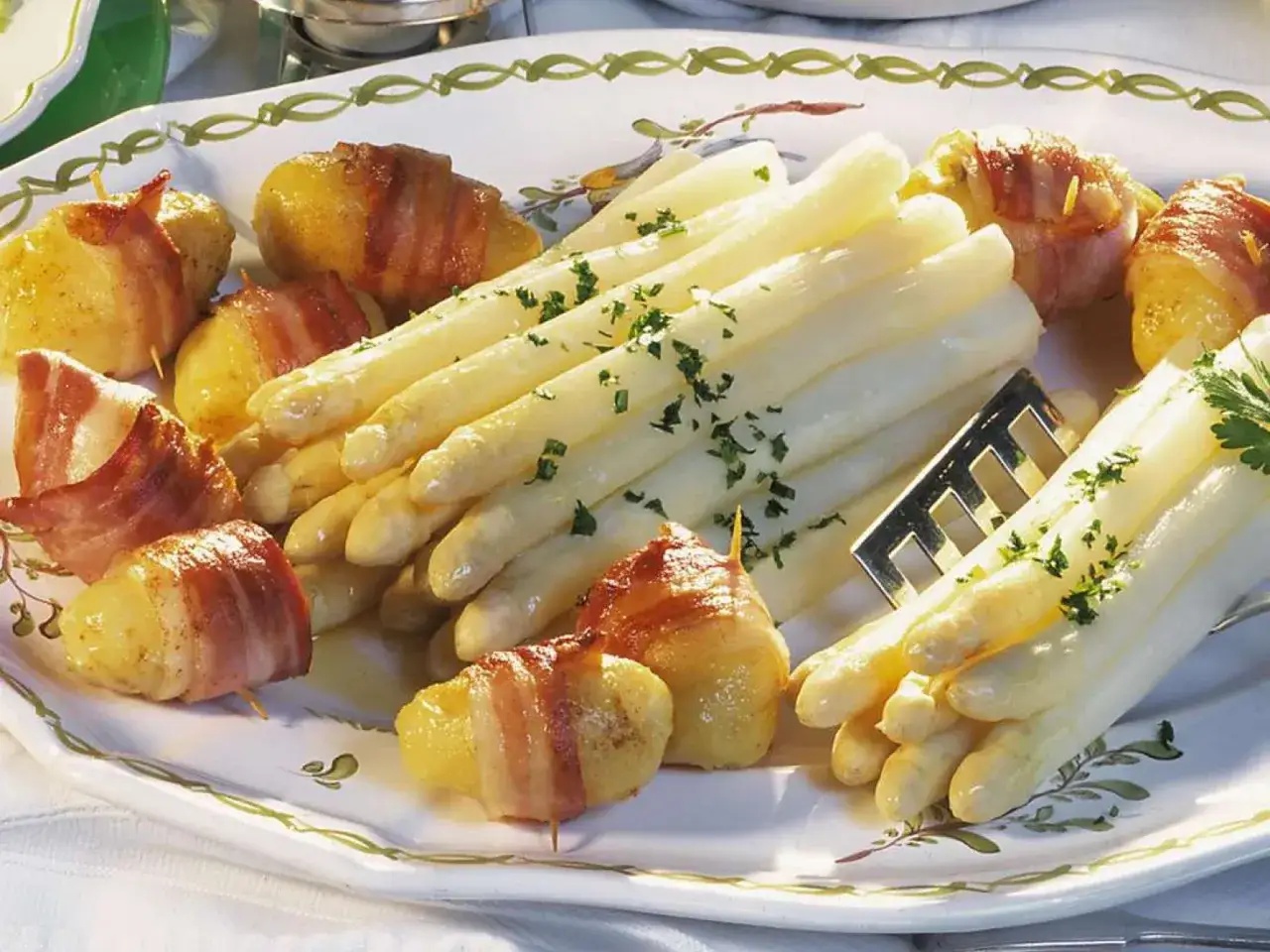 Ein Teller mit wei&szlig;em Spargel, garniert mit Petersilie, und Kartoffeln, umwickelt mit Speck. Eine k&ouml;stliche Spargel-Bowl f&uuml;r Genie&szlig;er.